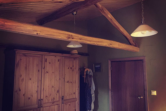 Esta fotografía pertenece a una reforma completa en donde se cambió por completo el aspecto de la misma. La estancia inicialmente presentaba techos excesivamente bajos, suelos muy fríos y una pésima distribución. Para reacondicionar esta estancia se elevó y aisló el techo (terminándolo con friso de abeto) eliminando desigualdades de los muros con paredes de pladur donde correspondía. También se trataron las vigas con anticarcoma, lijadas y tratadas con lasur. Se eliminó un armario empotrado que era el principal causante de la mala distribución. El suelo fue reacondicionado con tarima sintética flotante. También se presentó una nueva redistribución eléctrica haciendo más cómodo el uso de la habitación. El acabado de los muros fue realizado con pintura de teflón y un color que combinara con el friso de abeto. 